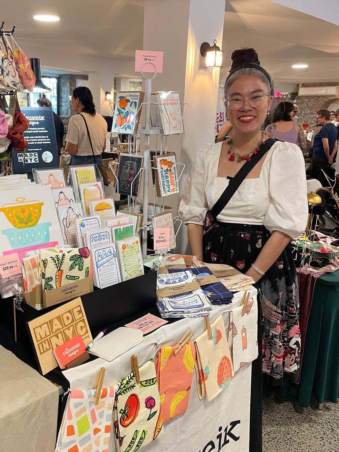 Winnie of Raisukeik Designs standing behind her craft fair table filled with products